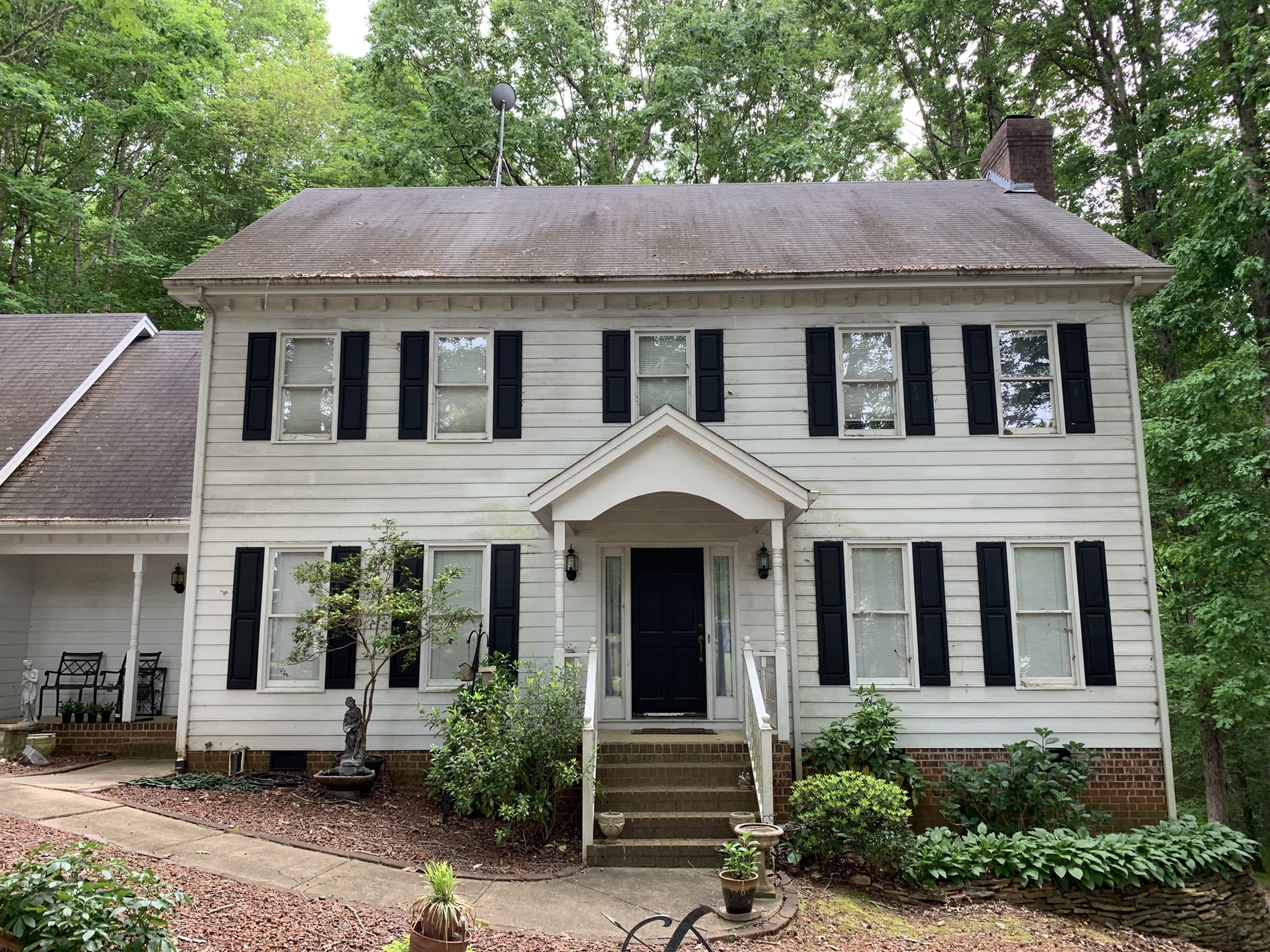 White two-story Raleigh home with black shutters and aging roof, ideal for Carolina siding, window, or roofing upgrades.