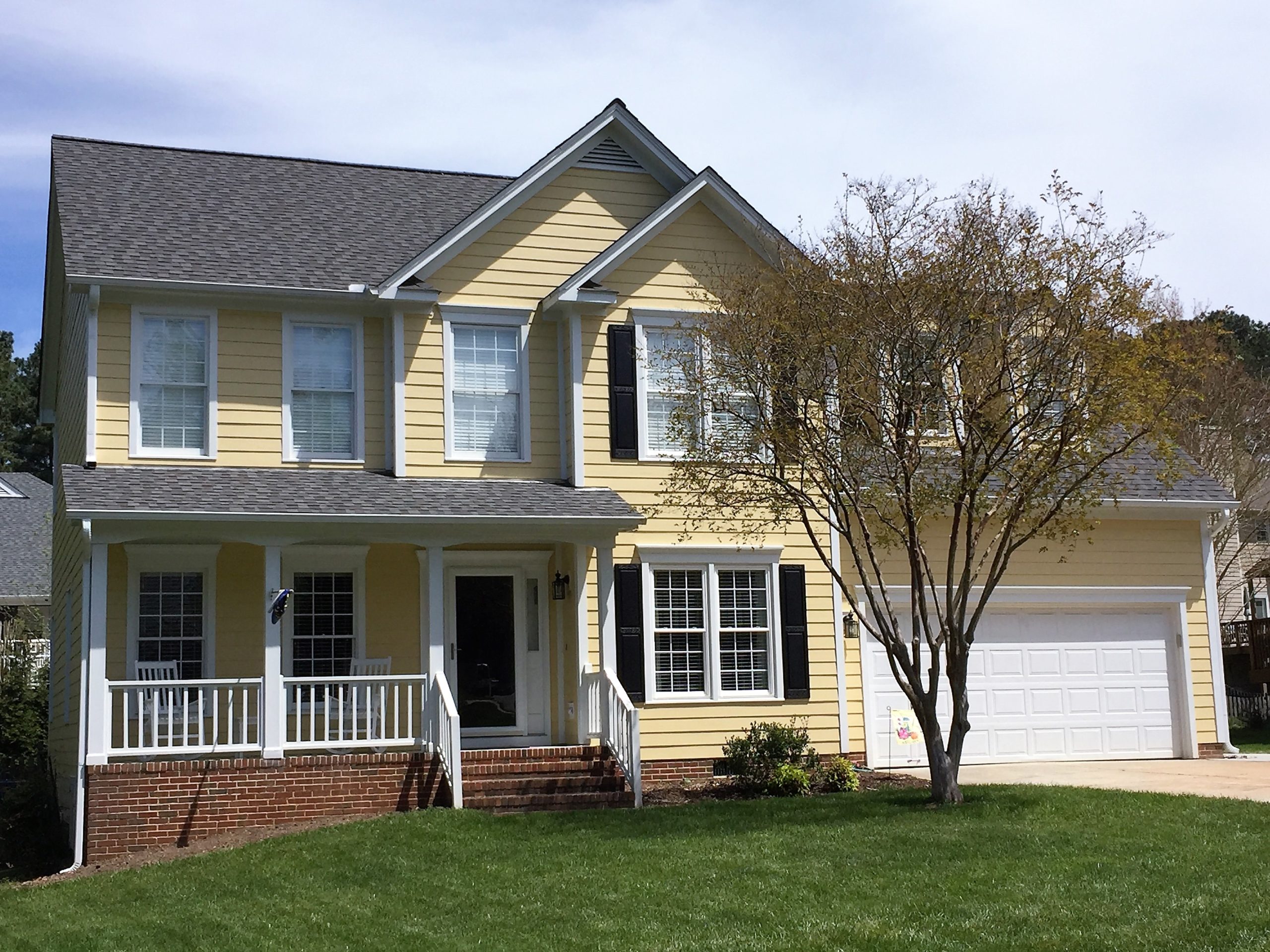 A two-story home with Harris Cream siding, white trim windows, a double garage, in Raleigh under blue skies and well-kept grass.