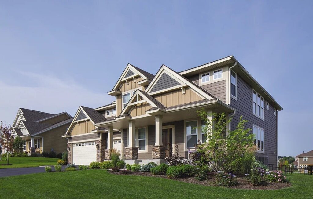 A two-story home with tan Carolina siding, white-trimmed windows, and a gabled roof in Raleigh, NC; manicured lawn and clear skies.